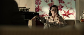 Movie still from “Department Q: The Absent One” (2014), directed by Mikkel Nørgaard – A woman sitting in front of a wall holding a bag; Medium shot, High angle