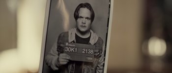 Movie still from “Department Q: The Absent One” (2014), directed by Mikkel Nørgaard – A black and white photo of a man holding a license plate; Close Up shot, High angle