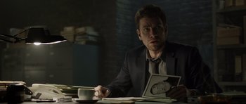 Movie still from “Department Q: The Absent One” (2014), directed by Mikkel Nørgaard – A man sitting at a table with a cup of coffee; Medium shot, Over the shoulder angle