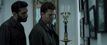 Movie still from “Department Q: The Absent One” (2014), directed by Mikkel Nørgaard – A man standing in front of a table with candles; Medium shot, Over the shoulder angle