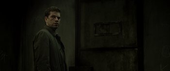 Movie still from “Department Q: The Absent One” (2014), directed by Mikkel Nørgaard – A man standing in front of a wall in a dark room; Medium shot, Low angle