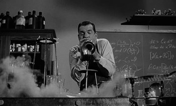 Movie still from “The Absent Minded Professor” (1961), directed by Robert Stevenson – A man in a science lab blowing into a device; Medium shot, Low angle