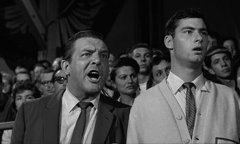 Movie still from “The Absent Minded Professor” (1961), directed by Robert Stevenson – A man in a crowd of people with his mouth wide open; Medium shot, Low angle