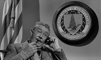 Movie still from “The Absent Minded Professor” (1961), directed by Robert Stevenson – An older man talking on a phone in front of a department of aging sign; Medium shot, Low angle