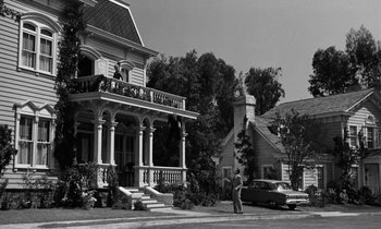 Movie still from “The Absent Minded Professor” (1961), directed by Robert Stevenson – An old photo of an old house with a man standing on the sidewalk; Wide shot, Low angle