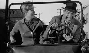 Movie still from “The Absent Minded Professor” (1961), directed by Robert Stevenson – An old photo of a man and a woman driving a car; Medium shot, Over the shoulder angle