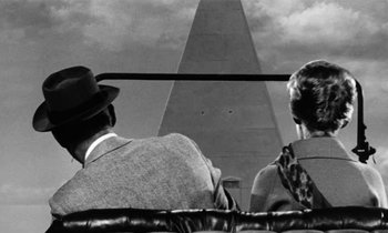 Movie still from “The Absent Minded Professor” (1961), directed by Robert Stevenson – A man and a woman sitting on a bench looking out at the sky; Medium shot, Low angle