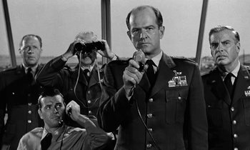 Movie still from “The Absent Minded Professor” (1961), directed by Robert Stevenson – A black and white photo of a man in uniform holding a microphone; Medium shot, Over the shoulder angle
