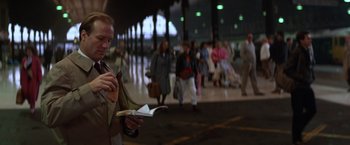 Movie still from “The Accidental Tourist” (1988), directed by Lawrence Kasdan – A man reading a magazine while standing in a crowd; Medium shot, Over the shoulder angle