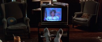 Movie still from “The Accidental Tourist” (1988), directed by Lawrence Kasdan – A person's feet on top of a table in front of a tv; Close Up shot, High angle