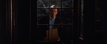 Movie still from “The Accidental Tourist” (1988), directed by Lawrence Kasdan – A man holding a piece of paper in front of a window; Medium shot, Low angle
