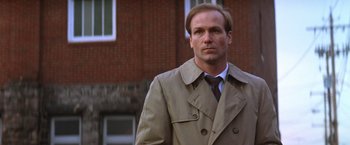 Movie still from “The Accidental Tourist” (1988), directed by Lawrence Kasdan – A man in a trench coat standing in front of a brick building; Close Up shot, Low angle