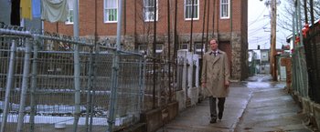 Movie still from “The Accidental Tourist” (1988), directed by Lawrence Kasdan – A man walking down the sidewalk in front of a brick building; Wide shot, Low angle