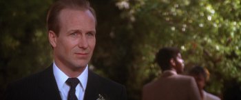 Movie still from “The Accidental Tourist” (1988), directed by Lawrence Kasdan – A man in a suit and tie standing in front of trees; Close Up shot, Over the shoulder angle