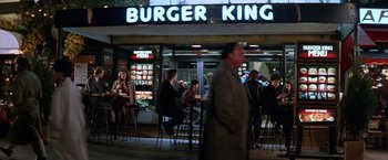 Movie still from “The Accidental Tourist” (1988), directed by Lawrence Kasdan – People sitting at tables outside of a burger king restaurant; Wide shot, High angle