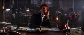 Movie still from “The Accidental Tourist” (1988), directed by Lawrence Kasdan – A woman sitting at a desk talking on a phone; Medium shot, Low angle