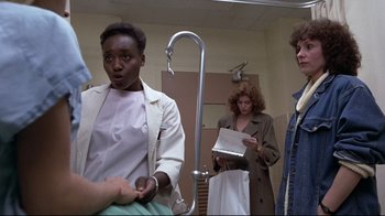 Movie still from “The Accused” (1988), directed by Jonathan Kaplan – A group of people standing in front of a bathroom mirror; Medium shot, Over the shoulder angle