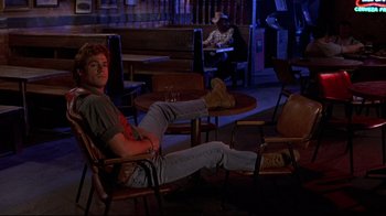 Movie still from “The Accused” (1988), directed by Jonathan Kaplan – A man sitting on a chair in a room; Wide shot, Low angle