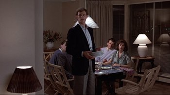 Movie still from “The Accused” (1988), directed by Jonathan Kaplan – A man standing in front of a table with a lamp on his head; Medium shot, Over the shoulder angle