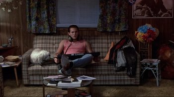 Movie still from “The Accused” (1988), directed by Jonathan Kaplan – A person sitting on a couch with a camera; Medium shot, High angle