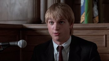 Movie still from “The Accused” (1988), directed by Jonathan Kaplan – A man in a suit and tie in front of a microphone; Close Up shot, Low angle