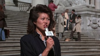 Movie still from “The Accused” (1988), directed by Jonathan Kaplan – A woman is holding a microphone while standing in front of stairs; Medium shot, Low angle