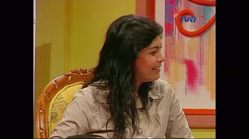 Movie still from “The Act of Killing” (2012), directed by Joshua Oppenheimer – A woman sitting in a chair smiling at the camera; Medium shot, High angle
