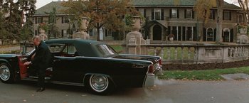 Movie still from “The Adjuster” (1991), directed by Atom Egoyan – An old car parked in front of a house; Wide shot, High angle