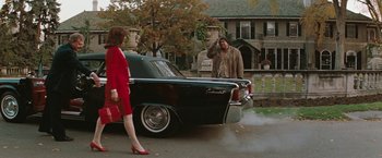 Movie still from “The Adjuster” (1991), directed by Atom Egoyan – A man and a woman standing in front of an old car; Wide shot, High angle