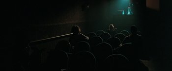 Movie still from “The Adjuster” (1991), directed by Atom Egoyan – A group of people sitting in a dark room; Wide shot, High angle