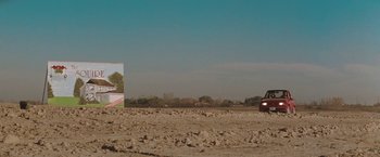 Movie still from “The Adjuster” (1991), directed by Atom Egoyan – A car driving down a dirt road next to an empty field; Extreme Wide shot, Low angle