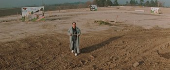 Movie still from “The Adjuster” (1991), directed by Atom Egoyan – A man standing in the middle of a dirt field; Extreme Wide shot, High angle