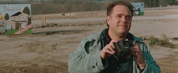 Movie still from “The Adjuster” (1991), directed by Atom Egoyan – A man taking a picture with a camera in a dirt field; Close Up shot, Low angle