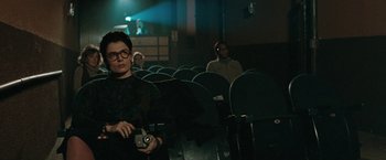 Movie still from “The Adjuster” (1991), directed by Atom Egoyan – A woman with a camera in a movie theater; Medium shot, Over the shoulder angle