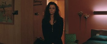 Movie still from “The Adjuster” (1991), directed by Atom Egoyan – A woman standing in front of a door in a room; Medium shot, High angle