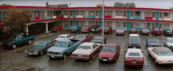 Movie still from “The Adjuster” (1991), directed by Atom Egoyan – A parking lot filled with parked cars next to a building; Extreme Wide shot, High angle