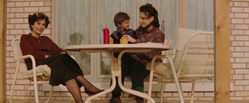 Movie still from “The Adjuster” (1991), directed by Atom Egoyan – A woman and a boy sitting at a table; Medium shot, High angle