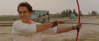 Movie still from “The Adjuster” (1991), directed by Atom Egoyan – A man holding a bow and arrow in his hands; Medium shot, Low angle