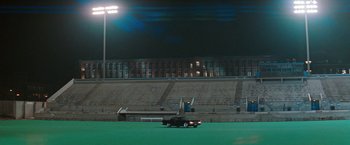Movie still from “The Adjuster” (1991), directed by Atom Egoyan – A truck is parked in a stadium field at night; Extreme Wide shot, High angle