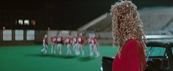 Movie still from “The Adjuster” (1991), directed by Atom Egoyan – A group of men in red shirts are playing football; Close Up shot, Over the shoulder angle