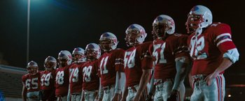 Movie still from “The Adjuster” (1991), directed by Atom Egoyan – A group of football players standing next to each other on a field; Wide shot, Low angle