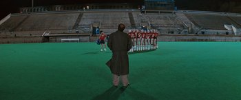 Movie still from “The Adjuster” (1991), directed by Atom Egoyan – A group of people standing on top of a green field; Wide shot, High angle