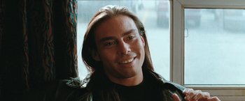 Movie still from “The Adjuster” (1991), directed by Atom Egoyan – A person wearing a leather jacket smiling; Close Up shot, Over the shoulder angle