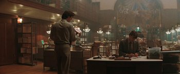 Movie still from “The Adjuster” (1991), directed by Atom Egoyan – A man standing in front of a desk in a room; Wide shot, Low angle