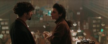 Movie still from “The Adjuster” (1991), directed by Atom Egoyan – A woman holding a coffee cup while standing next to another woman; Medium shot, Over the shoulder angle