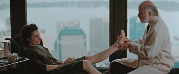 Movie still from “The Adjuster” (1991), directed by Atom Egoyan – Two women sitting on a couch with their feet up on the floor; Medium shot, Over the shoulder angle