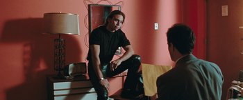 Movie still from “The Adjuster” (1991), directed by Atom Egoyan – A man sitting on a chair in a room; Medium shot, Over the shoulder angle