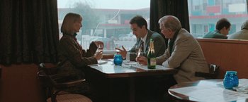 Movie still from “The Adjuster” (1991), directed by Atom Egoyan – A group of people sitting at a table with wine glasses; Medium shot, High angle