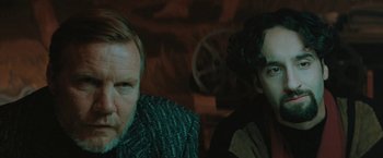 Movie still from “The Adjuster” (1991), directed by Atom Egoyan – Two people sitting in a room with a dark background; Close Up shot, Over the shoulder angle