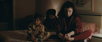 Movie still from “The Adjuster” (1991), directed by Atom Egoyan – A woman and two children sitting on a bed; Medium shot, Over the shoulder angle